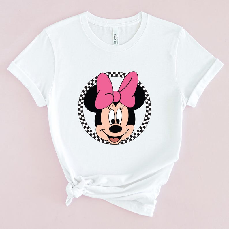Op de afbeelding: Wit T-shirt met een zwart-wit geblokte cirkel rond een cartoon afbeelding van Minnie Mouse met een roze strik.
