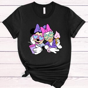 May include: Black t-shirt with a graphic of Minnie Mouse and Daisy Duck wearing heart-shaped sunglasses. Minnie is holding a purple drink and Daisy is holding an ice cream cone.