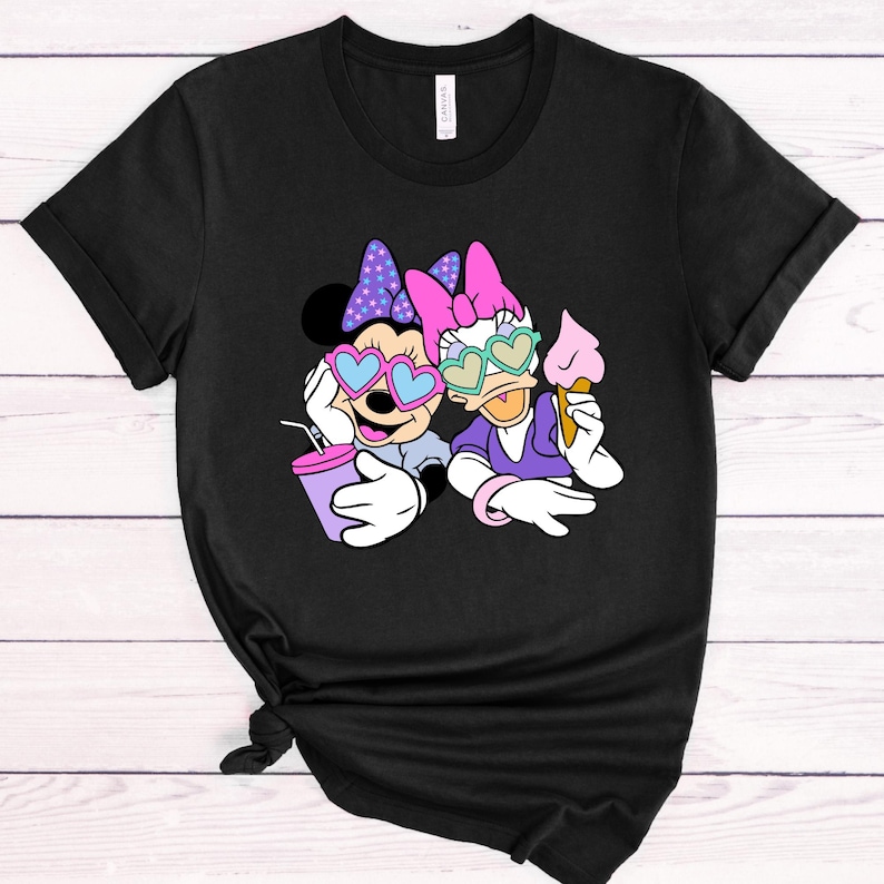 May include: Black t-shirt with a graphic of Minnie Mouse and Daisy Duck wearing heart-shaped sunglasses. Minnie is holding a purple drink and Daisy is holding an ice cream cone.