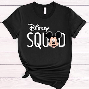 Puede incluir: Camiseta negra con la frase blanca "Disney SQUAD", el logo de Disney y un gr&aacute;fico de Mickey Mouse. La camiseta tiene mangas cortas y cuello redondo.
