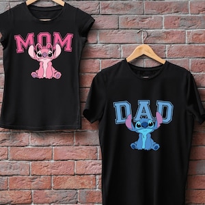 May include: Two black short-sleeved t-shirts. The left shirt features a pink cartoon character and the text MOM in pink block letters. The right shirt features a blue cartoon character and the text DAD in light blue block letters. Both shirts are on hangers.