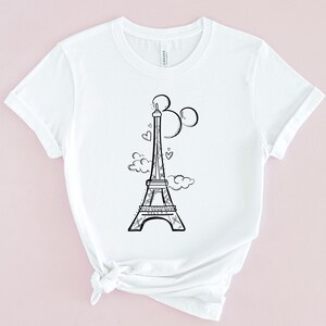 May include: White t-shirt featuring a black and white illustration of the Eiffel Tower with Mickey Mouse ears and hearts.