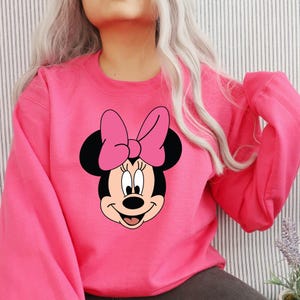 Peut inclure: Sweat-shirt rose avec un motif de Minnie Mouse portant un n&oelig;ud rose.