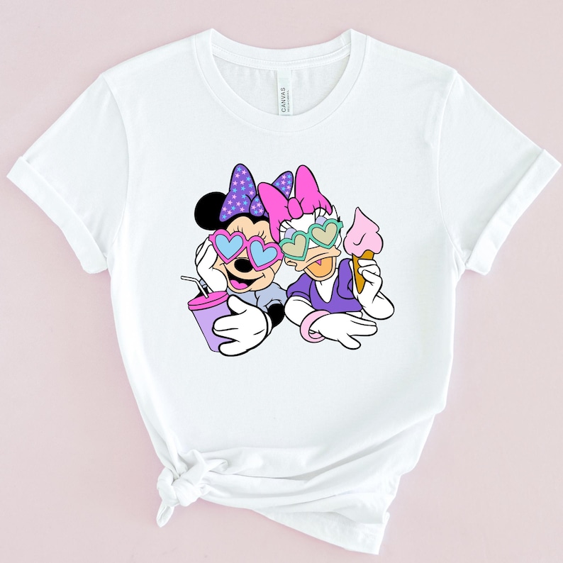 May include: White t-shirt with a graphic of Minnie Mouse and Daisy Duck wearing heart-shaped sunglasses. Minnie is holding a purple drink and Daisy is holding an ice cream cone.