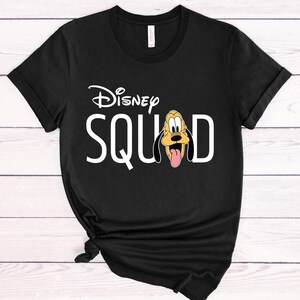 Puede incluir: Camiseta negra con la frase "Disney SQUAD" en blanco y el logotipo de Disney encima. La letra "D" es reemplazada por una imagen de Pluto. La camiseta est&aacute; anudada en la parte inferior. La camiseta es de algod&oacute;n.