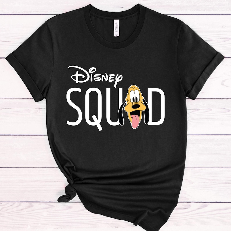 Puede incluir: Camiseta negra con la frase "Disney SQUAD" en blanco y el logotipo de Disney encima. La letra "D" es reemplazada por una imagen de Pluto. La camiseta est&aacute; anudada en la parte inferior. La camiseta es de algod&oacute;n.