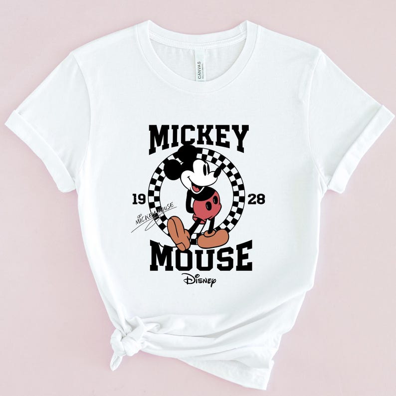 May include: White t-shirt with a black and white graphic of Mickey Mouse in a checkered circle. The text "Mickey Mouse" is above the graphic and "Disney" is below. The text "1928" is on the right side of the circle and "Mickey Mouse" is written in cursive on the left side of the circle.