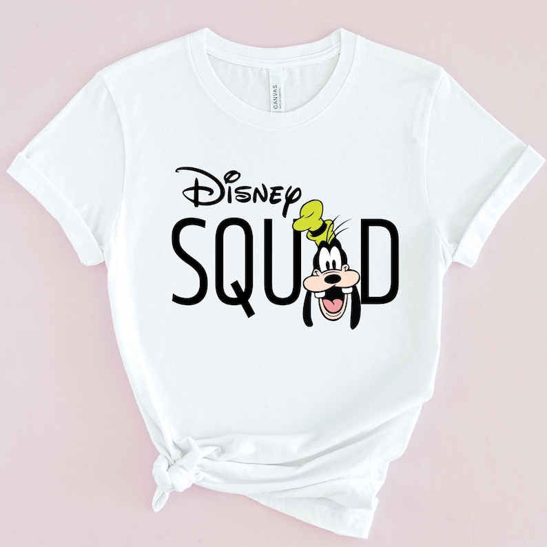 Puede incluir: Camiseta blanca con la frase "Disney SQUAD" en negro, con un dibujo de Goofy. El logo de Disney est&aacute; encima de la palabra "SQUAD". Goofy lleva su sombrero caracter&iacute;stico y tiene una gran sonrisa.