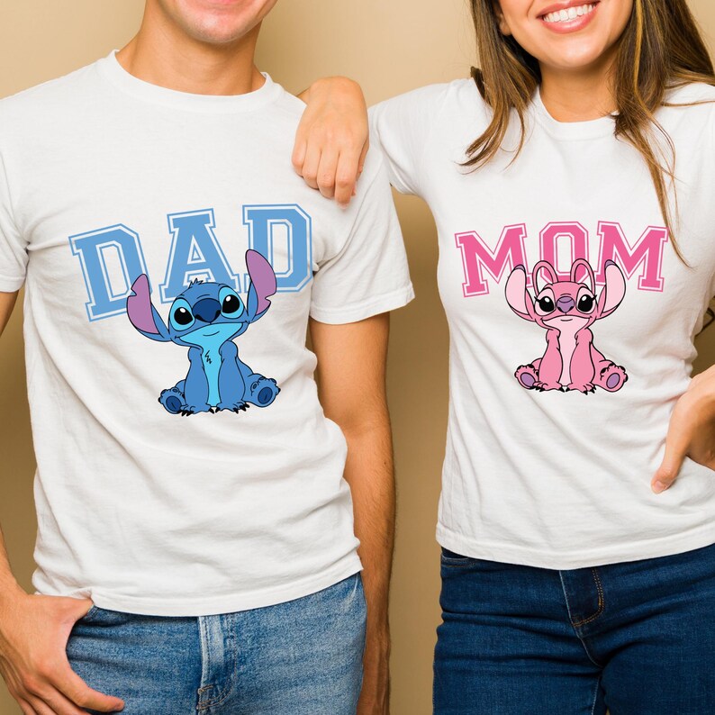 May include: Two white short-sleeved t-shirts. The left shirt features the blue text DAD with a blue Stitch character graphic. The right shirt features the pink text MOM with a pink Angel character graphic. Both shirts have a crew neckline.