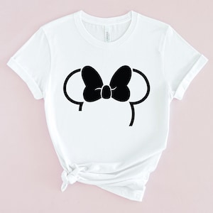 Puede incluir: Camiseta blanca con una silueta negra de las orejas y el lazo de Minnie Mouse.