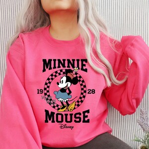 May include: Pink sweatshirt with a black and white graphic of Minnie Mouse. The graphic includes the text "Minnie Mouse" and "Disney".