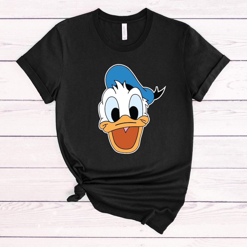 Peut inclure: T-shirt noir avec une image de dessin anim&eacute; du visage de Donald Duck. Donald Duck porte un chapeau de marin bleu.