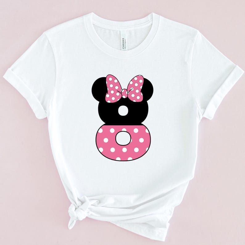 May include: White t-shirt featuring a black and pink graphic of a Minnie Mouse-inspired design. The design includes a black head with a pink polka dot bow, a black number 8, and a pink polka dot circle.
