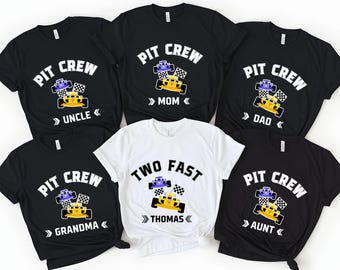 May include: A collection of black and white t-shirts with racing-themed designs. The shirts feature the words "PIT CREW" and a race car graphic. Some shirts have additional text like "UNCLE", "MOM", "DAD", "GRANDMA", and "AUNT". One white shirt says "TWO FAST" and "THOMAS".