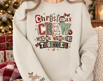 May include: A beige crewneck sweatshirt featuring a graphic with the text "Christmas CREW MAKING MEMORIES TOGETHER" in red, green, and white. The sleeve displays a small reindeer illustration above the name "Megan" in dark green script lettering.