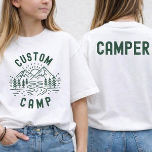 Personalized Camp Shirt With Mountain, Trees And River Design On Front And Bold Camper Text On Back, Custom Outdoor T Shirt For Family Camping Trip, Perfect For Nature Lovers And Group Adventure Outfit.