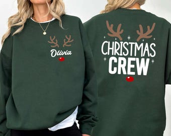 May include: Dark green sweatshirt featuring reindeer antlers, the name "Olivia", and a red nose graphic on the front. The back of the sweatshirt says "Christmas Crew" in white text with reindeer antlers and a red nose.