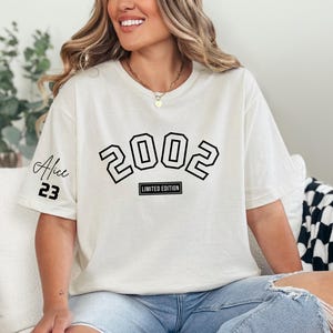 May include: White t-shirt with black text that says "2002 Limited Edition" and "Alice 23" on the sleeve.