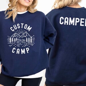 This personalized camp shirt is designed with a scenic mountain, forest, and river illustration, making it a great choice for nature lovers. Add your custom text to create a unique and memorable outfit for your camping experience.