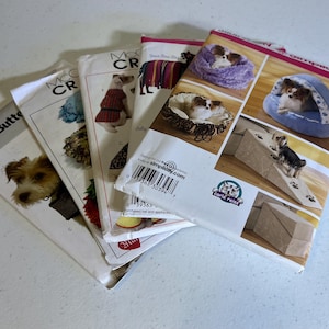 May include: A collection of dog sewing patterns, showing dogs in various outfits and dog beds. The patterns are from Butterick and McCall's. The patterns feature images of dog beds and ramps for pets.