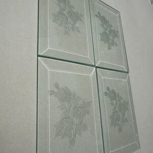 May include: Four rectangular glass panels with etched floral designs. Each panel features a detailed rose and leaf pattern, framed by a thin, etched border. The glass has a slightly frosted appearance, and the panels are arranged in a square formation.