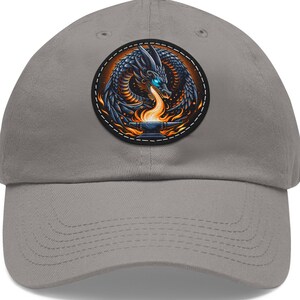 May include: A gray baseball cap featuring a circular patch with a detailed dragon design. The dragon is depicted in shades of blue and black, with fiery orange flames and a blue eye. The cap has a curved brim.