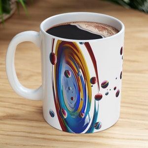 May include: White ceramic coffee mug with a colorful abstract design featuring a swirling pattern of blue, red, yellow, and orange. The design resembles a galaxy with small, colorful orbs scattered around the main swirl.