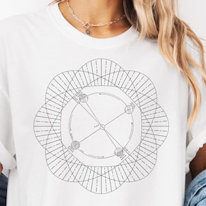 May include: White t-shirt with a black geometric design on the front. The design is a circular pattern with lines and shapes. The word "WHITE" is printed at the top. The shirt is paired with a denim jacket.