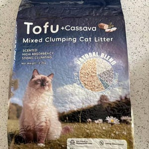 Op de afbeelding: Een donkerblauwe zak "Tofu + Cassava" gemengde klontvormende kattenbakvulling. De zak toont een kat en geeft aan dat het geparfumeerd is, sterk absorberend en sterk klonterend. Nettogewicht: 2,3 kg. De zak is milieuvriendelijk.