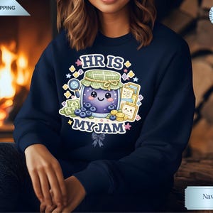 Peut inclure: Sweat-shirt bleu marine avec un motif de pot de confiture de dessin animé, avec un visage souriant, des myrtilles et le texte "HR IS MY JAM". Le motif comprend une loupe, de l'argent et des documents. Un style confortable et décontracté.