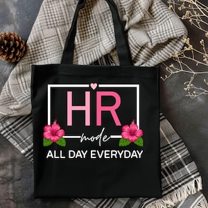 May include: Black tote bag with the text "HR mode ALL DAY EVERYDAY" in white. The letters "HR" are in pink, with a heart above the "R". Pink hibiscus flowers are on either side of the text. The bag has black handles.