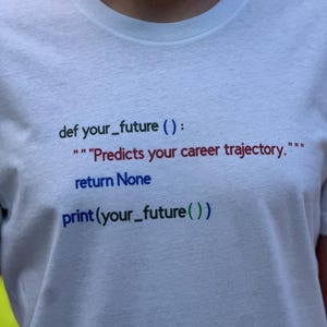 May include: White t-shirt with Python code printed in various colors. The text reads "def your_future():" followed by a quote about career trajectory, then "return None" and "print(your_future())".