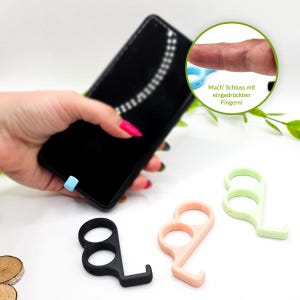 May include: A black smartphone held by a hand, with three different colored door opener tools. The tools are black, peach, and light green. The tools have a finger loop and a hook. A blue tool is attached to the phone. The text in the image says "Mach' Schluss mit eingedrückten Fingern!"