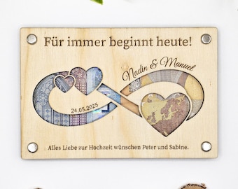 Op de afbeelding: Een houten bord met een oneindigheidssymbool gemaakt van eurobiljetten. Het bord zegt "Für immer beginnt heute!" en "Nadin & Manuel" met de datum "24.05.2025". Het bord zegt ook "Alles Liebe zur Hochzeit wünschen Peter und Sabine."