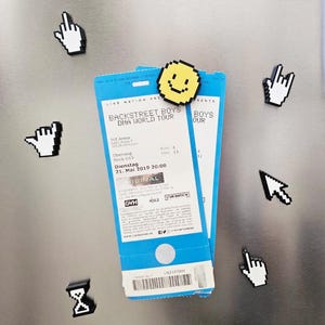 Puede incluir: Una colección de imanes pixelados con forma de cursores de ordenador, manos y una carita sonriente, junto con dos entradas azules para un concierto de los Backstreet Boys. Las entradas están sujetas por un imán de carita sonriente amarilla.