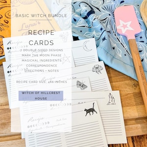 Op de afbeelding: Een Basic Witch Bundle met receptenkaarten van 10x15 cm met secties voor maanfasen, ingrediënten en notities. De kaarten tonen zwarte lijntekeningen van een kat, kaars, mot en onweerswolk. Een lichtblauwe doek met patroon en een roze spatel.