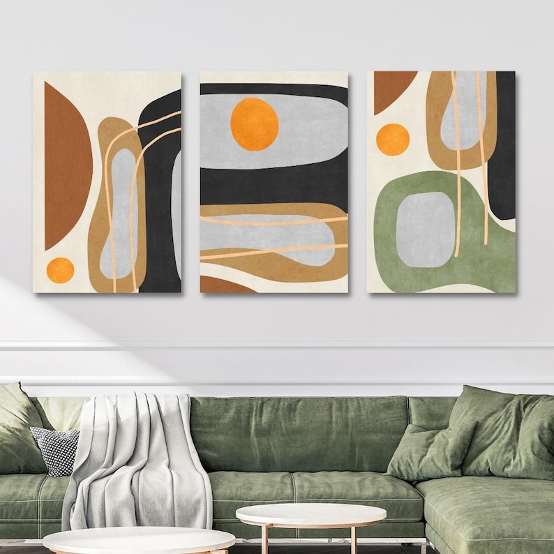 May include: Set of three abstract art prints. Each canvas features a unique design with geometric shapes in shades of brown, black, gray, and green, accented with orange circles and thin gold lines. The artwork is displayed above a green sofa.