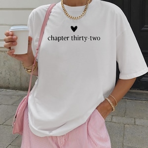 May include: White t-shirt with the text "chapter thirty-two" and a heart symbol. The shirt is paired with pink and white striped shorts. A gold chain necklace and bracelets are visible.