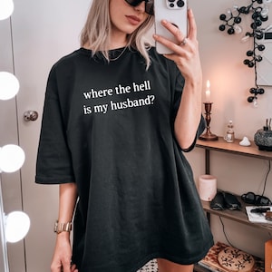 May include: Black oversized t-shirt with the text "where the hell is my husband?" printed in white. The shirt is worn with a black beanie and sunglasses.