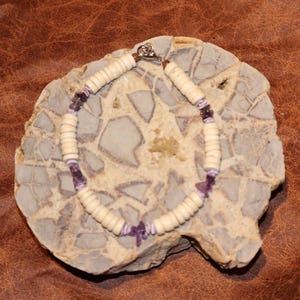 May include: A white and purple beaded bracelet with a silver clasp. The bracelet is made with small, round white beads and purple amethyst stones.
