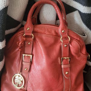 Bolso grande de piel naranja con diseño de trébol de 4 hojas, forro de satén, asas dobles desmontables, herrajes chapados en oro y dije.