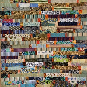 May include: A patchwork quilt with a variety of fabric patterns and colors. The quilt is made of rectangular strips of fabric sewn together horizontally. The fabrics include floral, striped, and geometric designs.