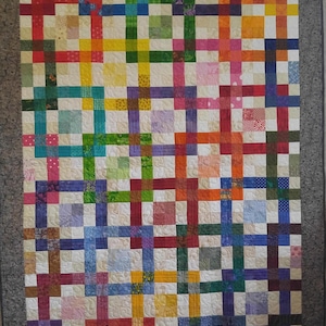 May include: A colourful quilt with a patchwork design featuring squares of various colours and patterns. The quilt is made up of a grid of squares, with each square containing a different fabric. The quilt is a vibrant and cheerful piece of art.