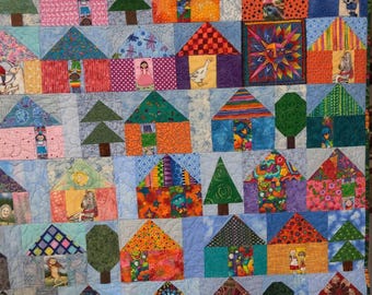May include: A colorful quilt with a patchwork design featuring houses, trees, and other whimsical patterns. The quilt is made up of various fabrics in shades of blue, green, pink, orange, and yellow.