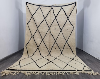 May include: Cream-colored rug with a bold black diamond pattern. The rug has a fringe along the bottom edge and is displayed against a neutral background. This geometric design rug is suitable for home decor.