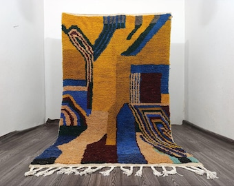 May include: A rectangular, hand-woven rug with a geometric design. The rug features a vibrant color palette of yellow, blue, brown, and beige. The design includes abstract shapes and lines. The rug has a fringe along the bottom edge.