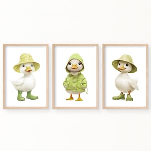 May include: Three framed prints featuring illustrations of ducks wearing different outfits. The first duck is wearing a green raincoat and a yellow hat. The second duck is wearing a green raincoat. The third duck is wearing a yellow hat.