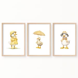 May include: Three framed prints featuring illustrations of a duck wearing a yellow raincoat, a duck holding a yellow and white checked umbrella, and a duck wearing a yellow and white checked hat and scarf.
