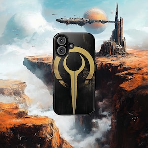 Könnte beinhalten: Schwarze Smartphone-Hülle mit einem goldenen Emblem-Design. Die Hülle befindet sich vor einer Science-Fiction-Landschaft mit einer futuristischen Stadt, Raumschiffen und einem Planeten im Hintergrund. Die Hülle hat ein Dual-Kamera-System.
