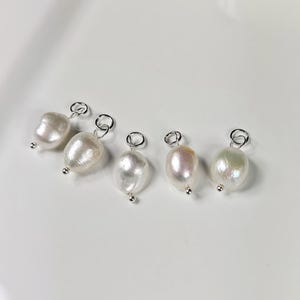 Könnte beinhalten: Fünf weiße Perlenanhänger mit silbernen Sprungringen. Die Perlen sind in verschiedenen Größen und Formen.